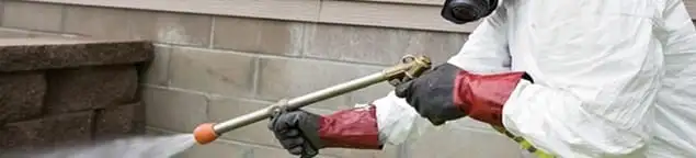 Pest control technician applying exterior insect treatment along a home foundation in Albuquerque, NM