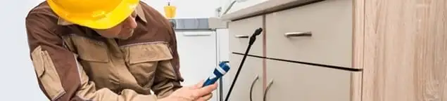 Roach exterminator applying treatment under kitchen cabinets in Albuquerque, NM