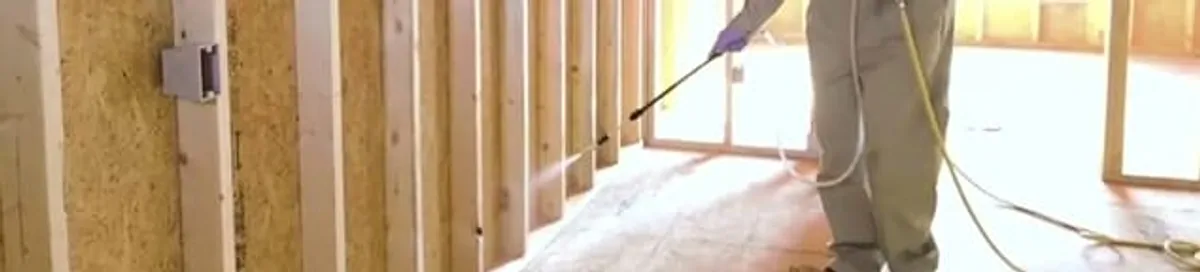 Termite treatment technician applying spray along framing and unfinished walls in Albuquerque, NM