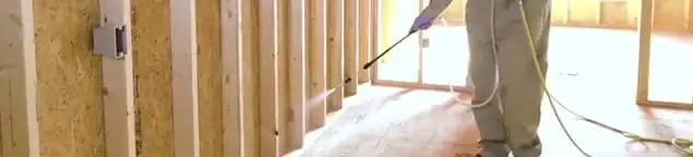 Termite treatment technician applying spray along framing and unfinished walls in Albuquerque, NM